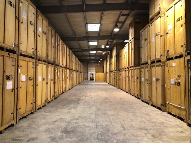 Allées centrales d’un garde-meuble avec des caisses en bois numérotées sur les côtés, stockage sécurisé et ample parcours.