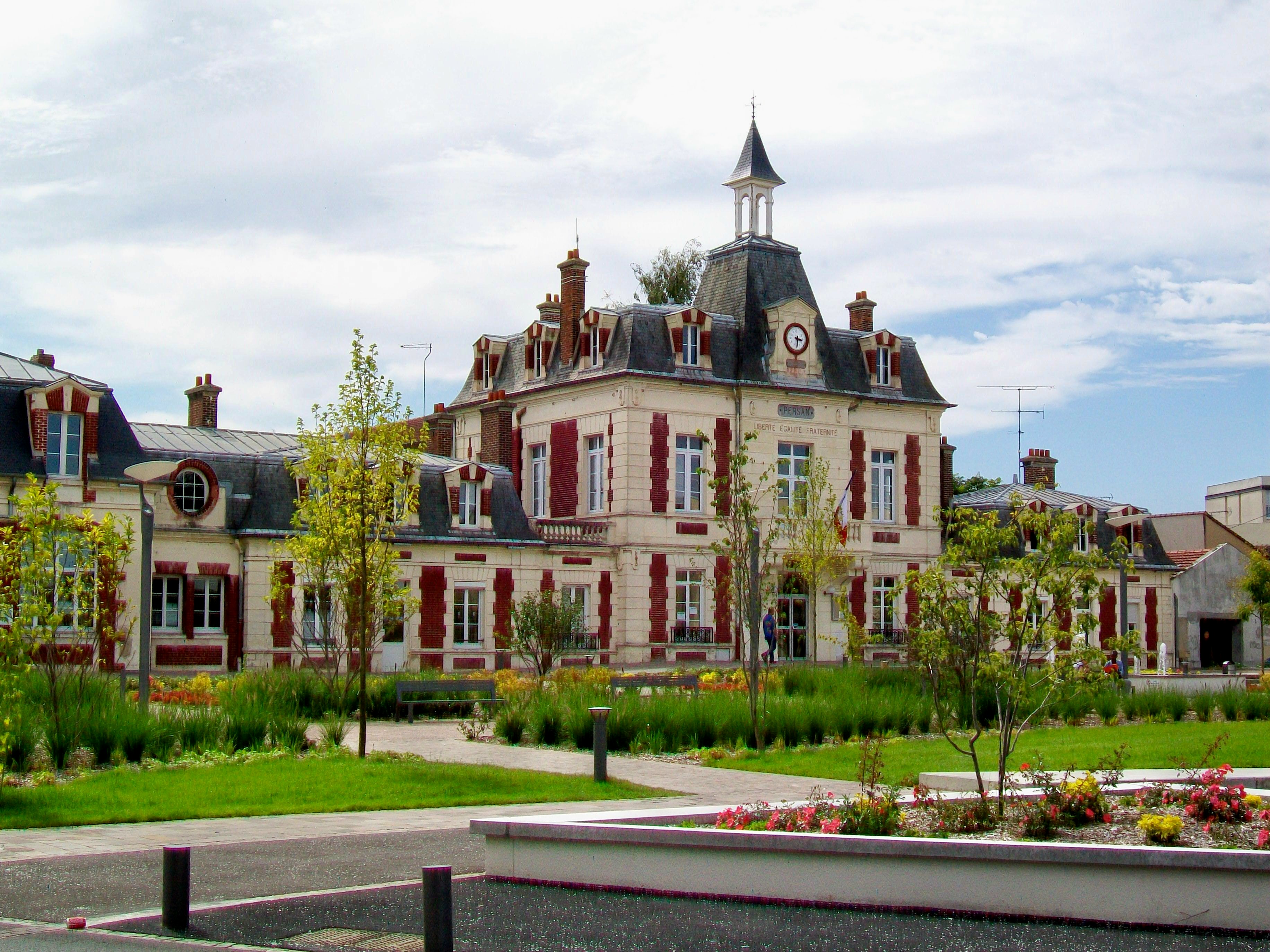 Immeuble communal classique avec façade claire et tourelles, entouré d’un parc verdoyant et de jardins.